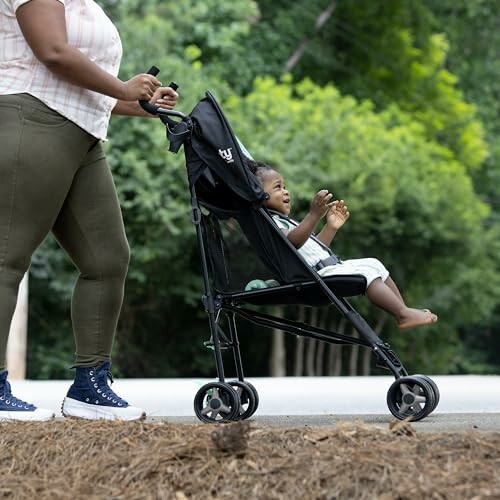 Adult pushing a baby in a stroller outdoors on a path.